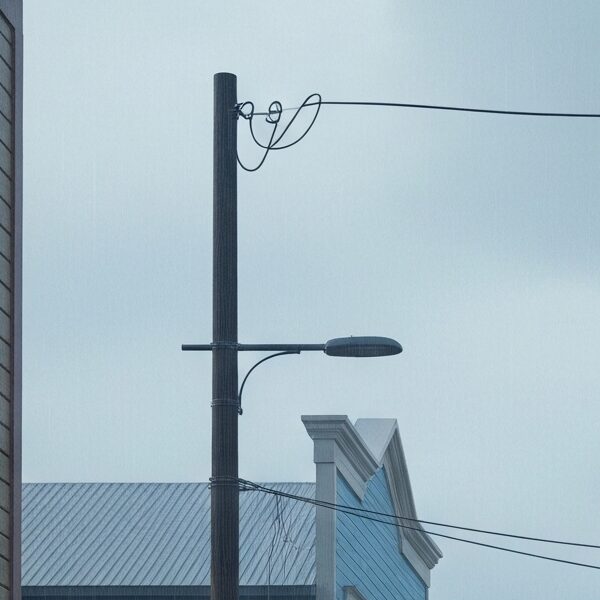 A melancholic, rain-soaked street in an alternate history Sitka, Alaska, reimagined as a Jewish settlement, with a lone figure walking towards a synagogue-like building under a cloudy sky.